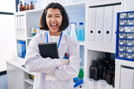 Photo for Young hispanic woman working at scientist laboratory celebrating crazy and amazed for success with open eyes screaming excited. - Royalty Free Image
