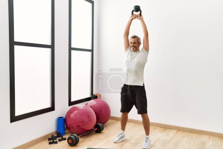 Photo for Middle age grey-haired man smiling confident using kettlebell training at sport center - Royalty Free Image