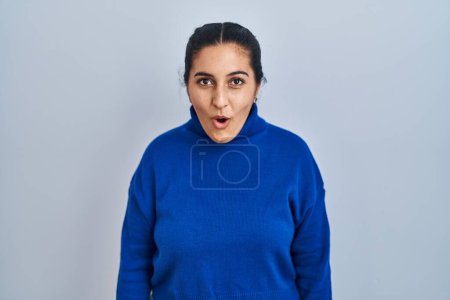 Foto de Mujer hispana joven de pie sobre un fondo aislado asustada y conmocionada por la sorpresa y la expresión asombrada, el miedo y la cara excitada. - Imagen libre de derechos