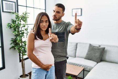 Téléchargez les photos : Jeune couple interracial attend un bébé, toucher le ventre enceinte pointant du doigt et l'expression en colère, ne montrant aucun geste - en image libre de droit