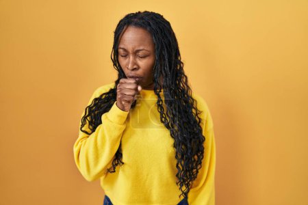 Téléchargez les photos : Femme africaine debout sur fond jaune se sentant mal à l'aise et toussant comme symptôme de rhume ou de bronchite. concept de soins de santé. - en image libre de droit