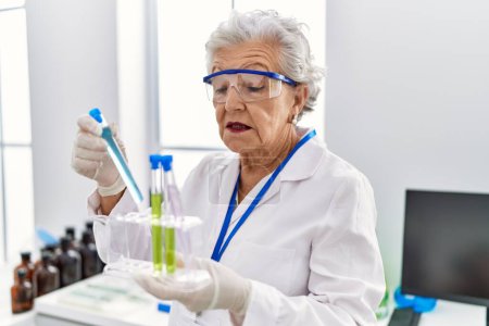 Foto de Mujer mayor de cabello gris con uniforme científico sosteniendo tubos de ensayo en el laboratorio - Imagen libre de derechos