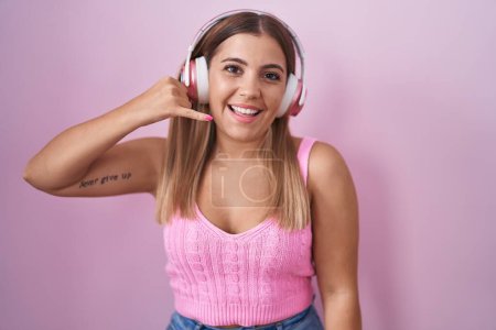 Photo for Young blonde woman listening to music using headphones smiling doing phone gesture with hand and fingers like talking on the telephone. communicating concepts. - Royalty Free Image