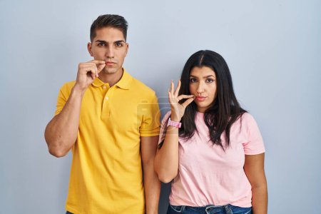 Téléchargez les photos : Young couple standing over isolated background mouth and lips shut as zip with fingers. secret and silent, taboo talking - en image libre de droit