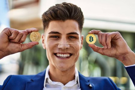 Téléchargez les photos : Jeune homme souriant confiant tenant Bitcoin et ethereum à la rue - en image libre de droit