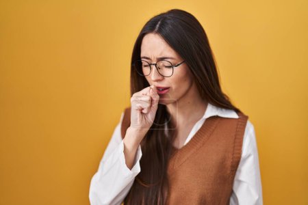 Photo for Young brunette woman standing over yellow background wearing glasses feeling unwell and coughing as symptom for cold or bronchitis. health care concept. - Royalty Free Image