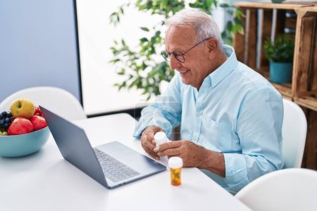 Photo for Senior grey-haired man having telemedicine sitting on table at home - Royalty Free Image