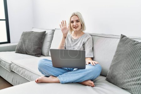 Photo for Young caucasian woman using laptop at home sitting on the sofa showing and pointing up with fingers number five while smiling confident and happy. - Royalty Free Image