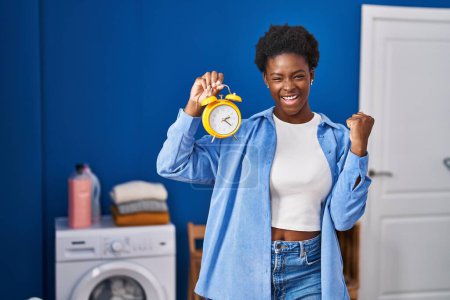 Photo for African american woman waiting for laundry screaming proud, celebrating victory and success very excited with raised arms - Royalty Free Image