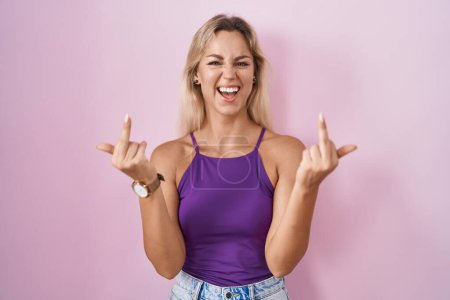 Foto de Young blonde woman standing over pink background showing middle finger doing fuck you bad expression, provocation and rude attitude. screaming excited - Imagen libre de derechos