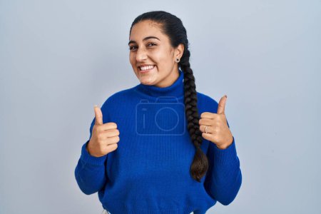 Photo for Young hispanic woman standing over isolated background success sign doing positive gesture with hand, thumbs up smiling and happy. cheerful expression and winner gesture. - Royalty Free Image