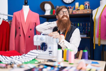Photo for Young redhead man tailor stressed using sewing machine at clothing factory - Royalty Free Image