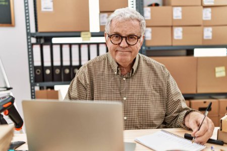 Photo for Middle age grey-haired man using laptop and writing on notebook working at storehouse - Royalty Free Image