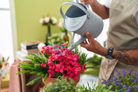 Téléchargez les photos : Jeune homme latin fleuriste arrosage plante à la boutique de fleurs - en image libre de droit