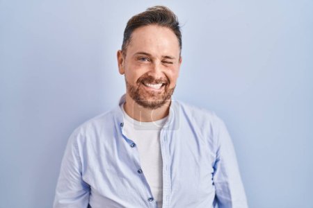 Photo for Middle age caucasian man standing over blue background winking looking at the camera with sexy expression, cheerful and happy face. - Royalty Free Image