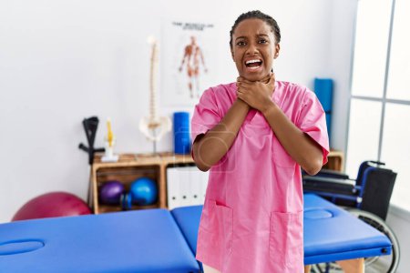 Foto de Mujer afroamericana joven que trabaja en la clínica de recuperación del dolor gritando y sofocándose por estrangulamiento doloroso. problema de salud. concepto de asfixia y suicidio. - Imagen libre de derechos
