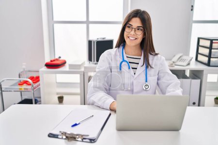 Téléchargez les photos : Jeune belle hispanique femme médecin en utilisant un ordinateur portable travaillant à la clinique - en image libre de droit