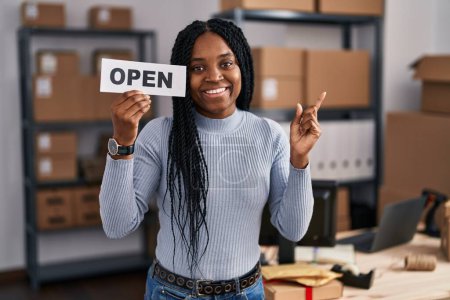Foto de Mujer afroamericana que trabaja en el comercio electrónico de pequeñas empresas sosteniendo pancarta abierta sonriendo feliz señalando con la mano y el dedo a un lado - Imagen libre de derechos