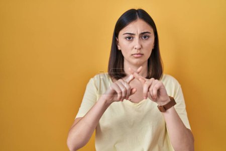 Téléchargez les photos : Hispanic girl wearing casual t shirt over yellow background rejection expression crossing fingers doing negative sign - en image libre de droit