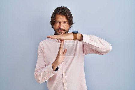 Foto de Guapo hombre de mediana edad con elegante camisa de fondo haciendo tiempo fuera gesto con las manos, frustrado y cara seria - Imagen libre de derechos