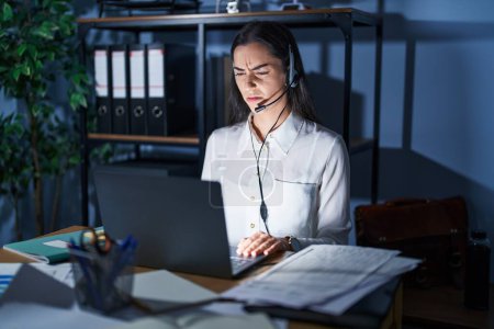 Photo for Young brunette woman wearing call center agent headset working late at night skeptic and nervous, frowning upset because of problem. negative person. - Royalty Free Image