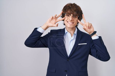 Photo for Hispanic business young man wearing glasses doing peace symbol with fingers over face, smiling cheerful showing victory - Royalty Free Image