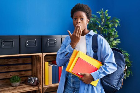 Photo for African american woman wearing student backpack and holding books covering mouth with hand, shocked and afraid for mistake. surprised expression - Royalty Free Image