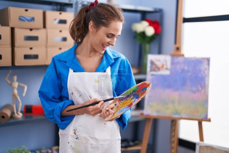 Photo for Young woman artist holding paintbrush and palette at art studio - Royalty Free Image