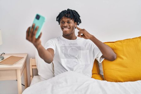 Téléchargez les photos : Young african man with dreadlocks taking a selfie on the bed smiling happy pointing with hand and finger - en image libre de droit