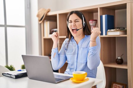 Photo for Young brunette woman wearing call center agent headset very happy and excited doing winner gesture with arms raised, smiling and screaming for success. celebration concept. - Royalty Free Image