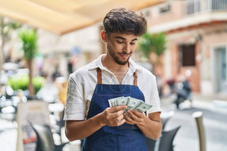 Photo for Young arab man waiter counting dollars working at restaurant - Royalty Free Image
