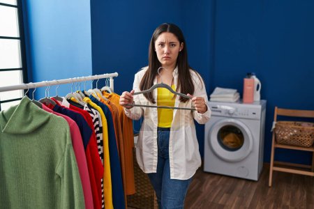 Photo for Young latin woman putting clean laundry on hangers skeptic and nervous, frowning upset because of problem. negative person. - Royalty Free Image