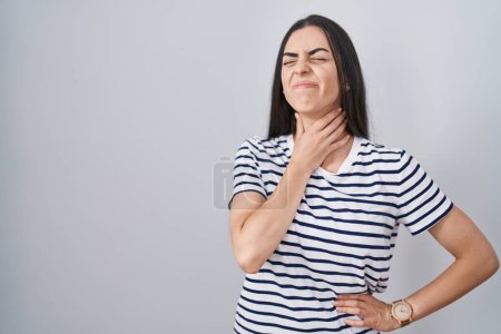 Foto de Mujer morena joven con camiseta rayada tocando el cuello doloroso, dolor de garganta para la gripe, la clod y la infección - Imagen libre de derechos