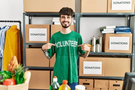 Téléchargez les photos : Jeune homme hispanique pointant vers l'uniforme bénévole travaillant au centre de charité. - en image libre de droit