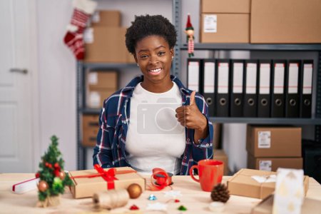 Photo for African american woman working at small business doing christmas decoration doing happy thumbs up gesture with hand. approving expression looking at the camera showing success. - Royalty Free Image