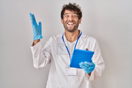 Photo for Hispanic scientist man working with tablet celebrating victory with happy smile and winner expression with raised hands - Royalty Free Image