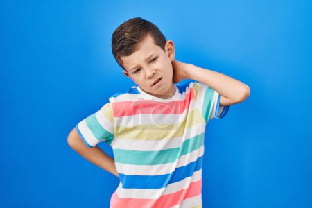 Photo for Young caucasian kid standing over blue background suffering of neck ache injury, touching neck with hand, muscular pain - Royalty Free Image
