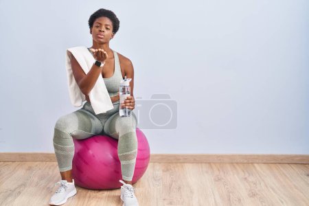 Photo for African american woman wearing sportswear sitting on pilates ball looking at the camera blowing a kiss with hand on air being lovely and sexy. love expression. - Royalty Free Image