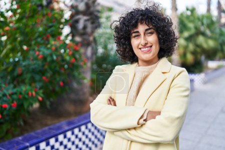 Foto de Joven mujer de Oriente Medio excusa sonriente confiado de pie con los brazos cruzados gesto en el parque - Imagen libre de derechos