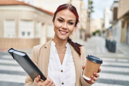 Photo for Young caucasian woman business worker drinking coffee holding binder at street - Royalty Free Image