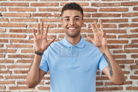 Photo for Brazilian young man standing over brick wall showing and pointing up with fingers number nine while smiling confident and happy. - Royalty Free Image