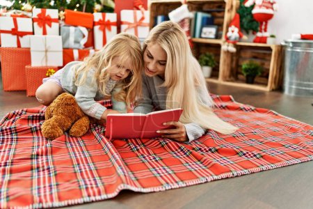 Téléchargez les photos : Mère et fille lisant le livre couché près de l'arbre de Noël à la maison - en image libre de droit