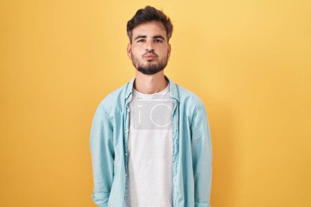 Photo for Young hispanic man with tattoos standing over yellow background looking at the camera blowing a kiss on air being lovely and sexy. love expression. - Royalty Free Image