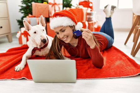 Téléchargez les photos : Young caucasian woman holding credit card lying with dog by christmas tree at home - en image libre de droit