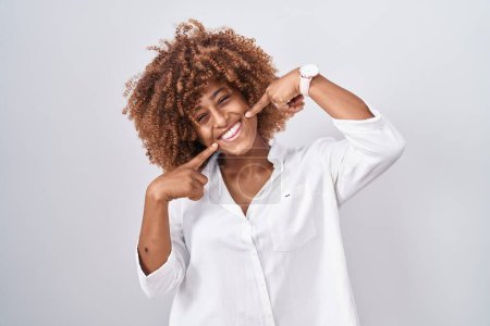 Téléchargez les photos : Young hispanic woman with curly hair standing over white background smiling cheerful showing and pointing with fingers teeth and mouth. dental health concept. - en image libre de droit