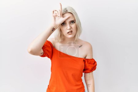 Photo for Young caucasian woman standing over isolated background making fun of people with fingers on forehead doing loser gesture mocking and insulting. - Royalty Free Image
