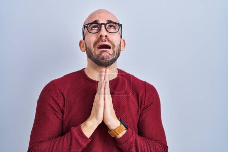 Photo for Young bald man with beard standing over white background wearing glasses begging and praying with hands together with hope expression on face very emotional and worried. begging. - Royalty Free Image