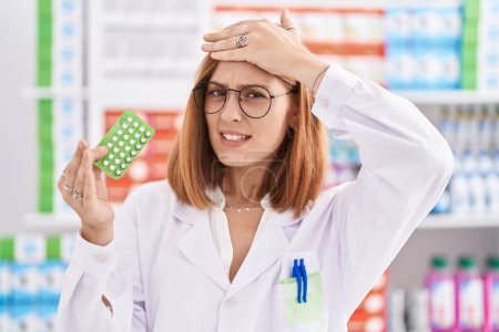 Photo for Young redhead woman working at pharmacy drugstore holding birth control pills stressed and frustrated with hand on head, surprised and angry face - Royalty Free Image