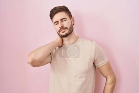 Foto de Hispanic man with beard standing over pink background suffering of neck ache injury, touching neck with hand, muscular pain - Imagen libre de derechos