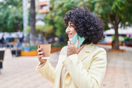 Téléchargez les photos : Jeune femme du Moyen-Orient excutive parler sur le smartphone boire du café au parc - en image libre de droit